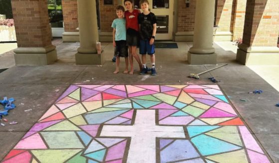 Children stand behind a chalk cross, which is set against a drawing of a stained-glass window outside of the governor's mansion in Arkansas.