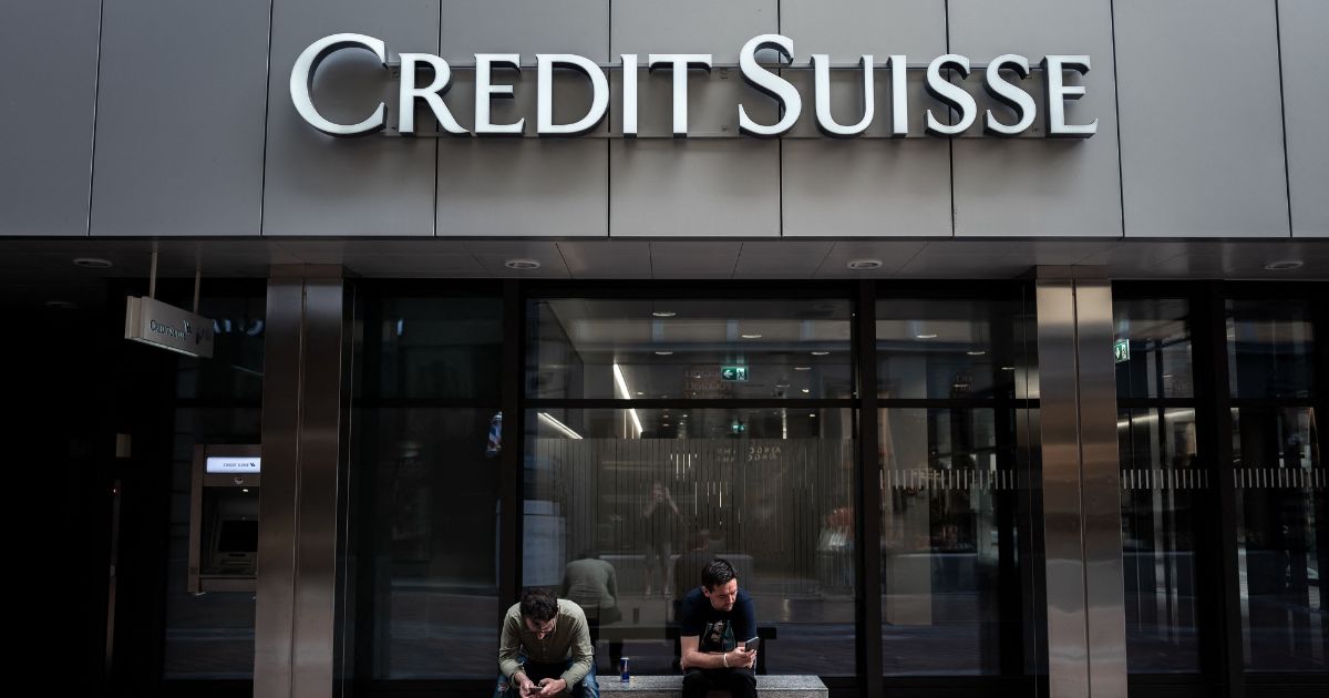 Two men sit under a sign of Credit Suisse displayed on a building in Lugano, on June 9.