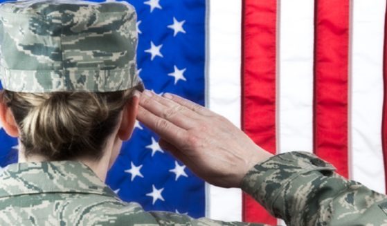 A female soldier viewed from behind saluting the American flag.