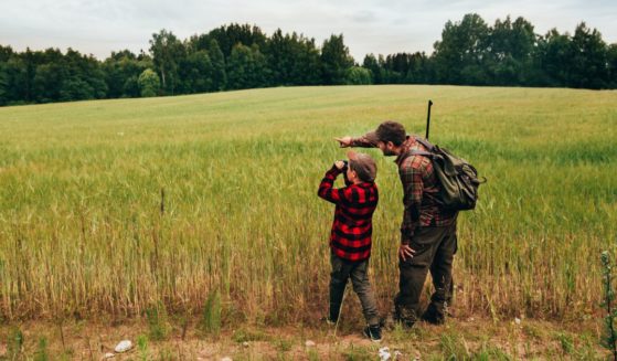 A father and son are pictured hunting for boar in an open grass area. Moments like these may come more rarely, as the Biden administration passed a new law prohibiting youth hunting and archery classes at school from receiving federal funding.