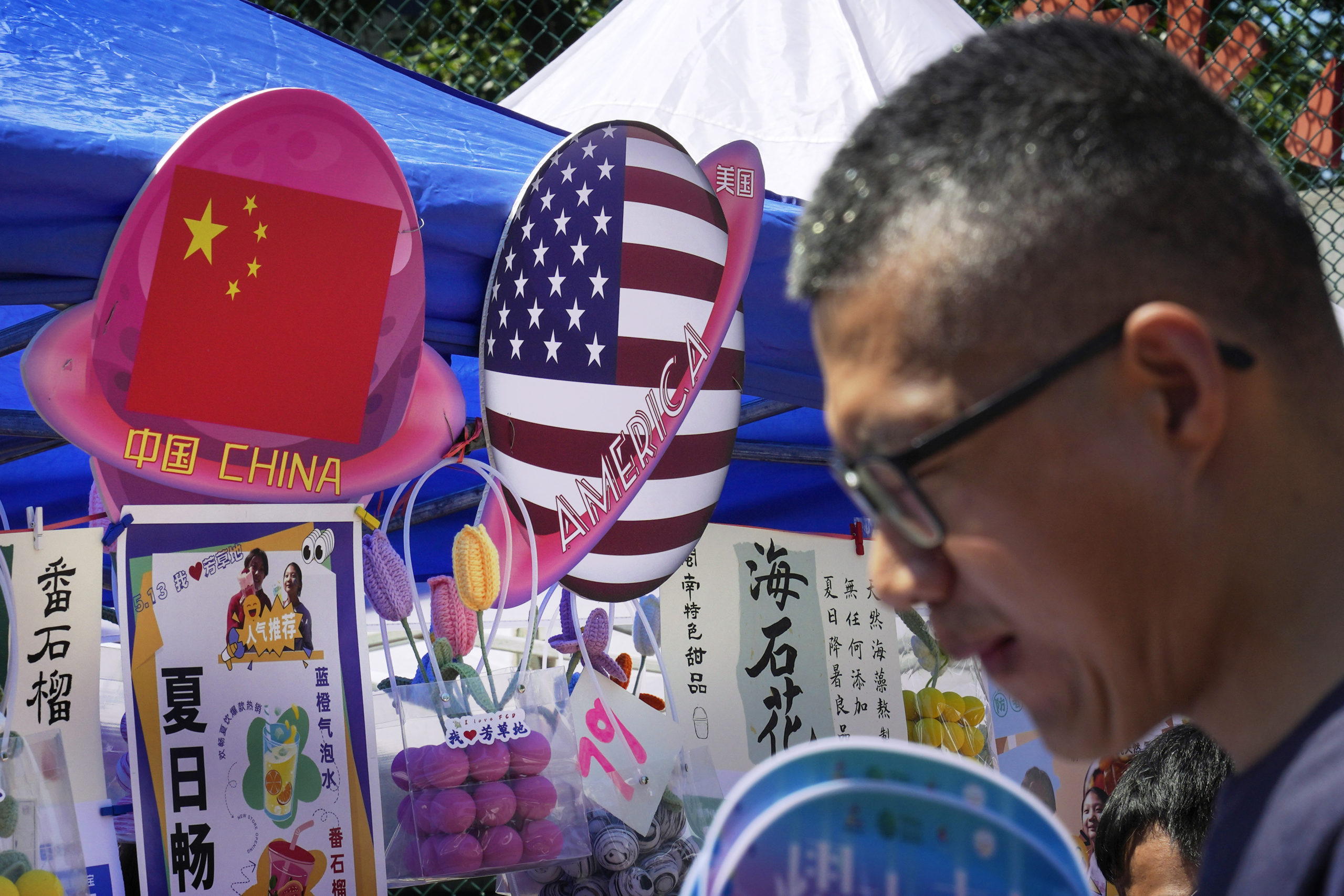 A man walks by a booth selling foods and beverages displaying planet-shaped flags of China and the U.S. during a spring carnival in Beijing on May 13. China has detained a worker from a military group on suspicion of spying for the CIA.