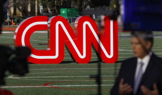 a reporter records video near a CNN sign on an athletic field