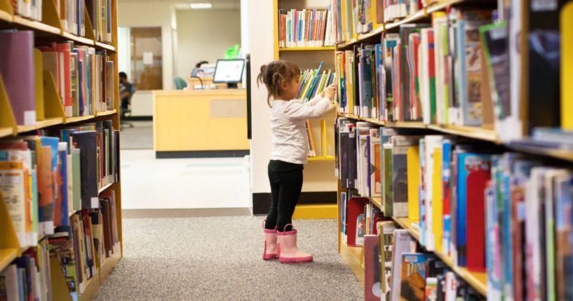 A little girl in preschool visits her library to select books to read.