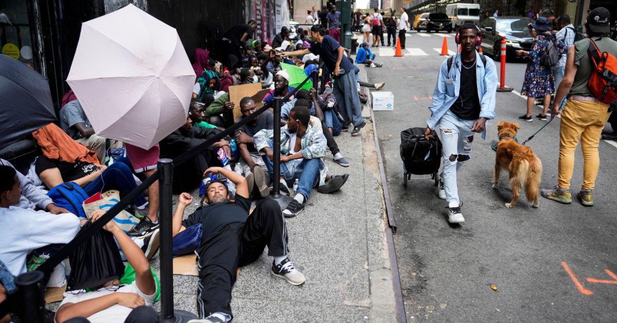 Migrants sit in a queue outside of The Roosevelt Hotel in New York City on July 31. The hotel is being used by the city as temporary housing.