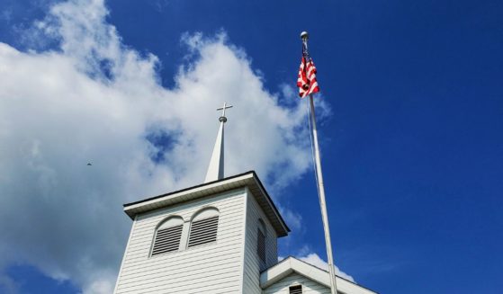 The American flag flies next to a church steeple in this stock image.