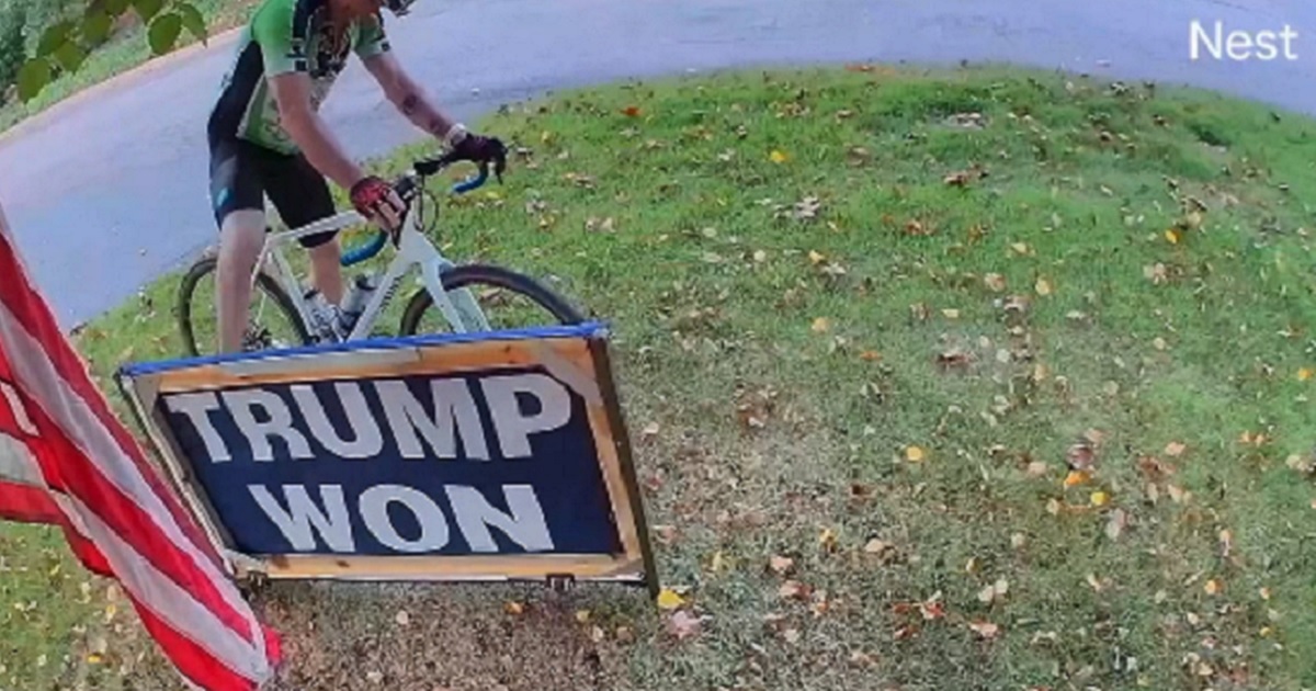 A cyclist kicks a "Trump won" sign on a lawn in a still from a surveillance video.