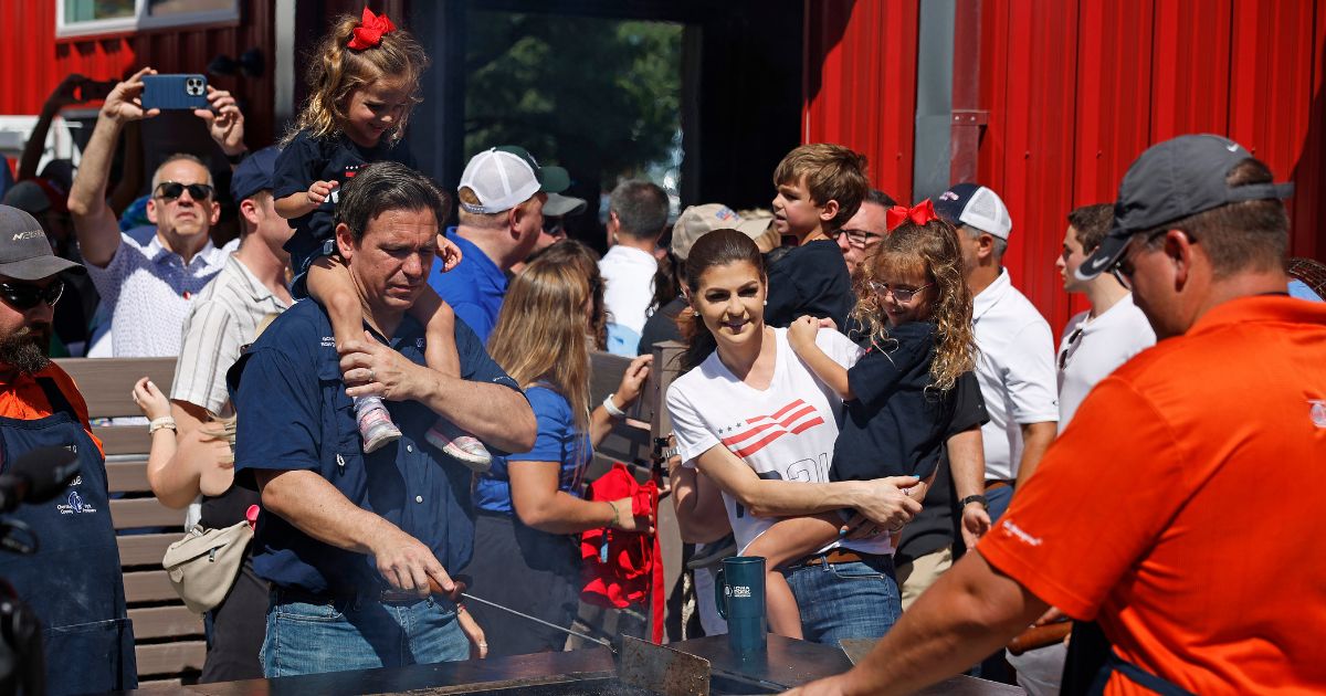 With daughter Mamie, 3, on his shoulders, Florida Governor and Republican presidential candidate Ron DeSantis and his wife Casey DeSantis holding their daughter Madison, 6, work the grill at the Iowa Pork Producers Tent at the Iowa State Fair on Aug. 12 in Des Moines, Iowa.