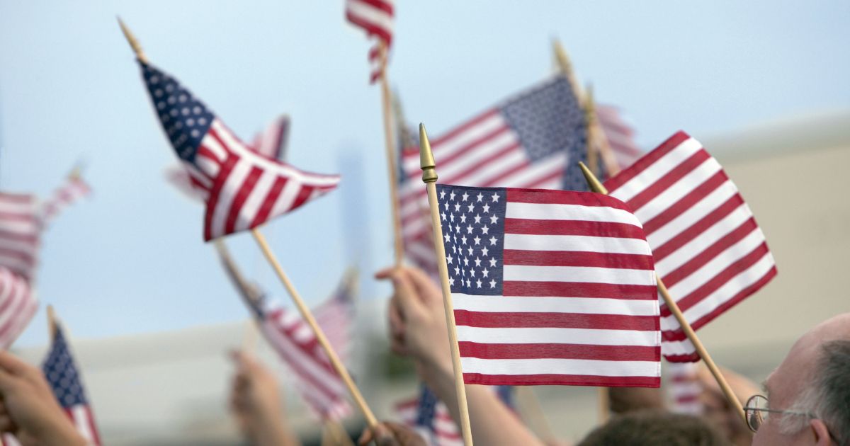 A crowd waves American flags in the above stock image.