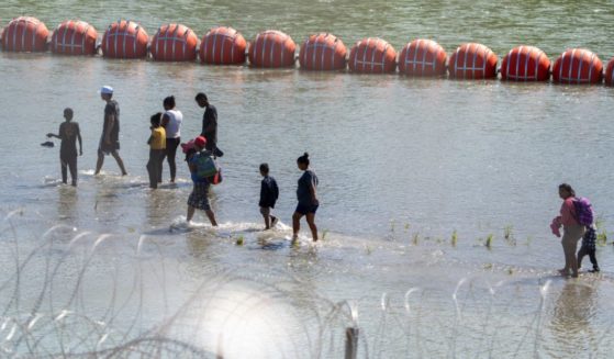 Migrants walk by a string of buoys placed on the water along the Rio Grande border with Mexico in Eagle Pass, Texas, on July 15 to prevent illegal immigration entry to the U.S.