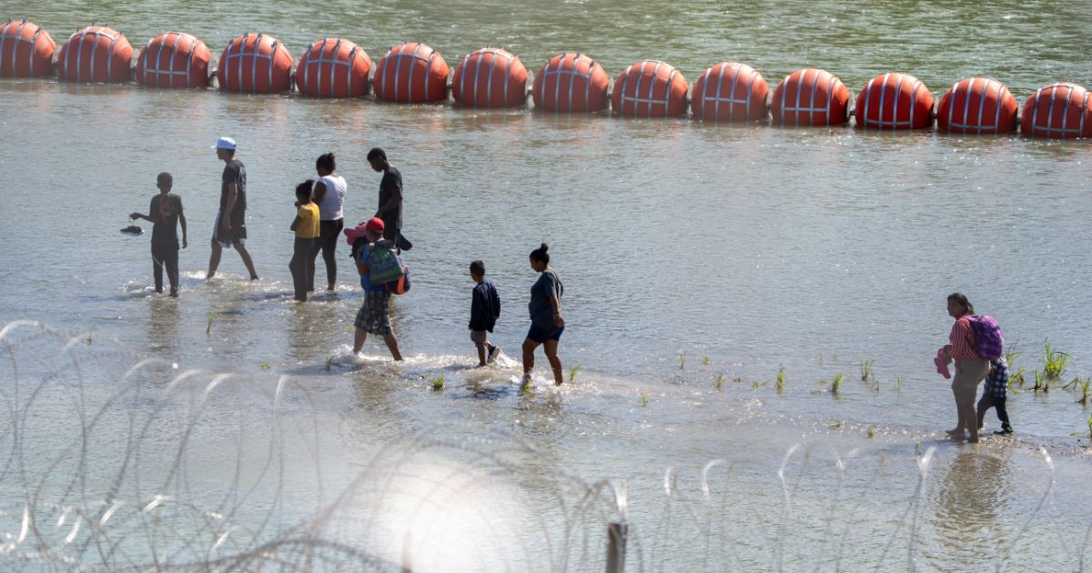 Migrants walk by a string of buoys placed on the water along the Rio Grande border with Mexico in Eagle Pass, Texas, on July 15 to prevent illegal immigration entry to the U.S.