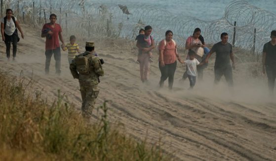 A Texas guardsman watches as migrants, who crossed the Rio Grande from Mexico to the U.S., walk along concertina wire, on Monday, in Eagle Pass, Texas.