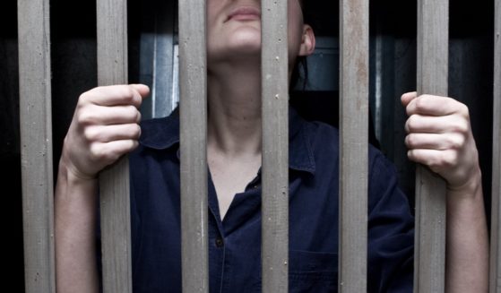 A stock photo of a woman behind bars.