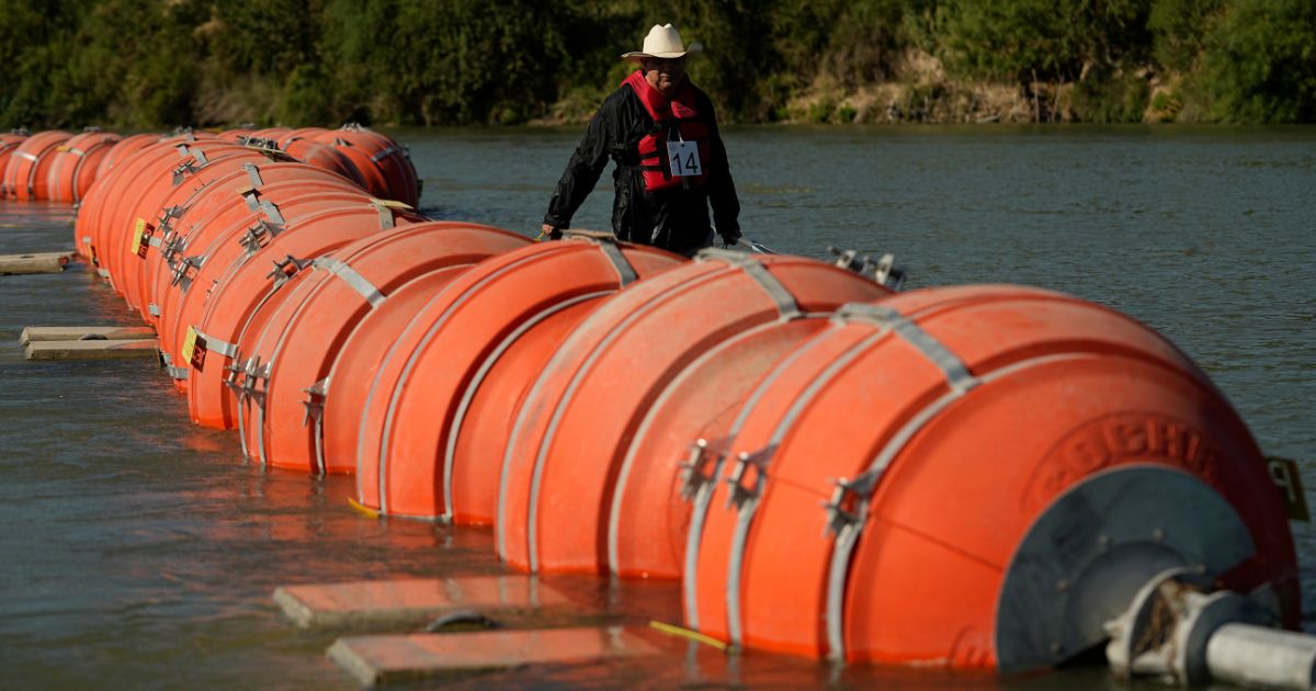 A kayaker walks past large buoys being used as a floating border barrier on the Rio Grande in Eagle Pass, Texas, on Aug. 1.
