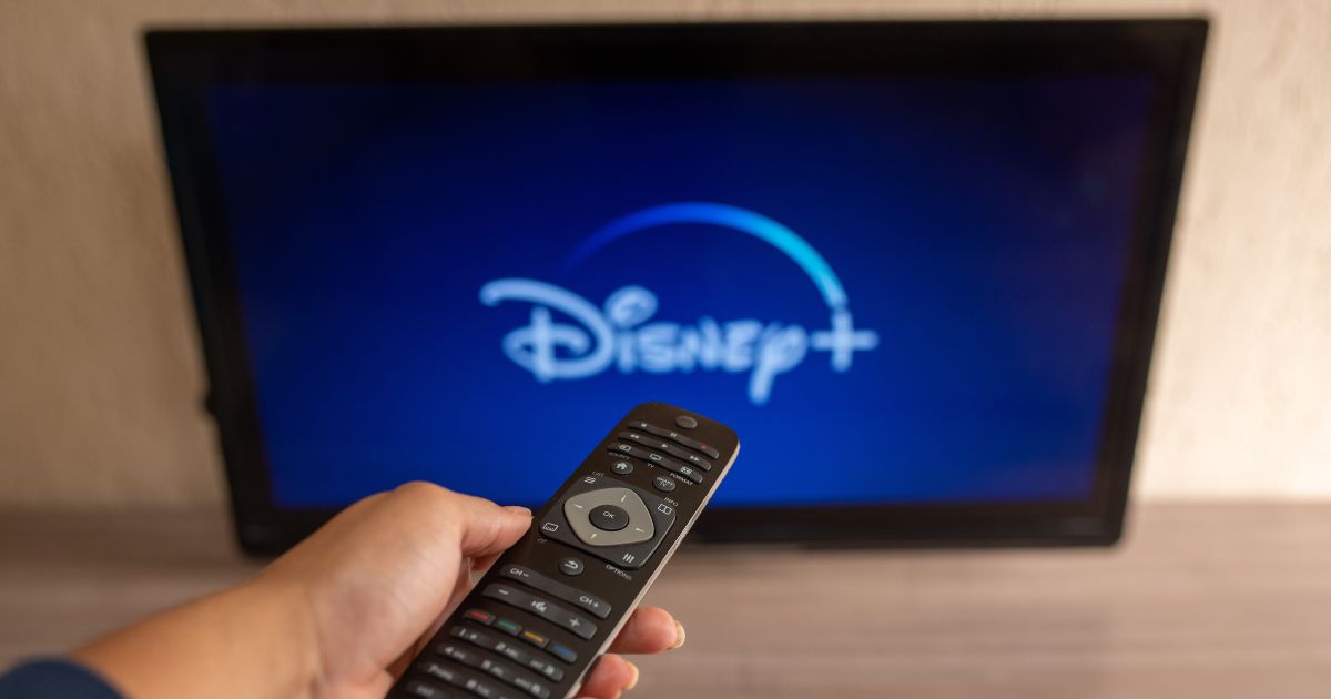 A stock photo shows a remote control pointing at a television with the Disney+ streaming service on the screen.