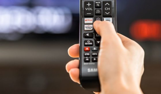 A stock photo shows a hand holding a Samsung television remote control featuring streaming channels such as Netflix and Amazon Prime Video.