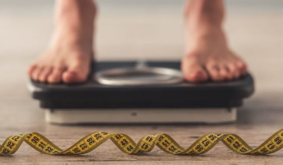 A person stands on a scale with a tape measure in front of it. With the obesity epidemic in America, many people shouldn't qualify to serve in the military due to their weight.