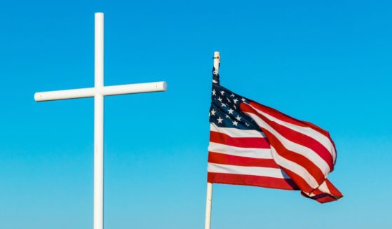 An American flag flies next to a cross in the above stock image.