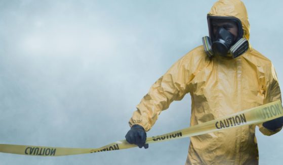 This stock image shows a worker in a hazmat suit putting up caution tape.