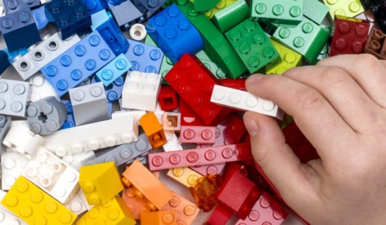 A child's and holds a Lego brick over a pile of Lego bricks.