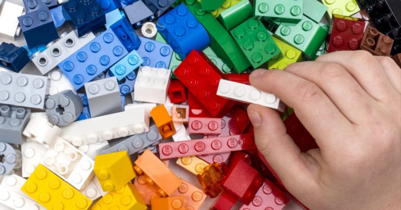 A child's and holds a Lego brick over a pile of Lego bricks.