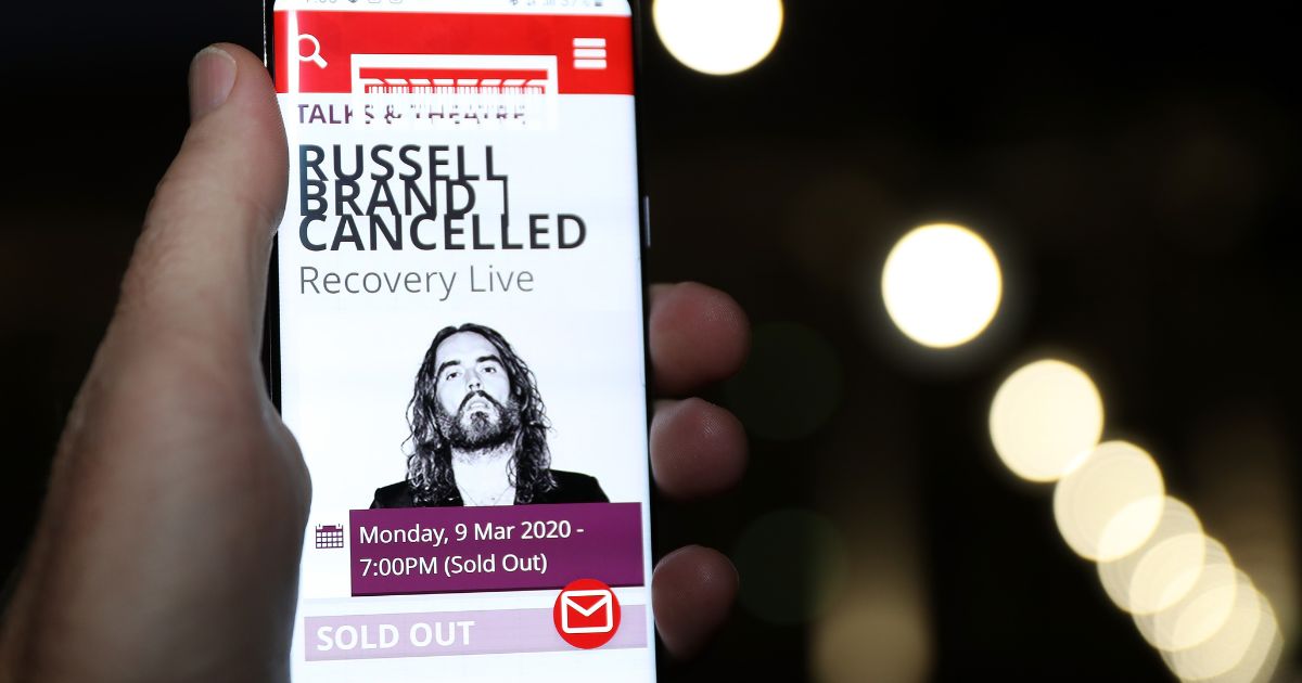 In this photo illustration the web page for the Perth Concert Hall is displayed on a mobile phone advising of the cancelled Russell Brand show on March 9, 2020 in Perth, Australia.