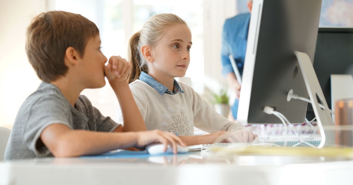 A stock photo shows children working on a desktop computer in a school computer lab.
