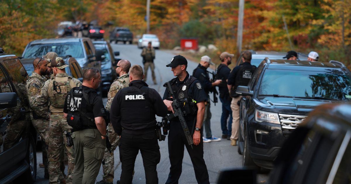 Law enforcement officials gather in the road leading to the home of the suspect being sought in connection with two mass shootings on Thursday in Bowdoin, Maine.