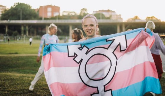 A girl holds up a flag with the transgender symbol in front of other children at a park. A federal court recently ruled that Iowa's Linn-Mar School District cannot force students and teachers to "respect" gender pronouns as it violates their First Amendment rights.