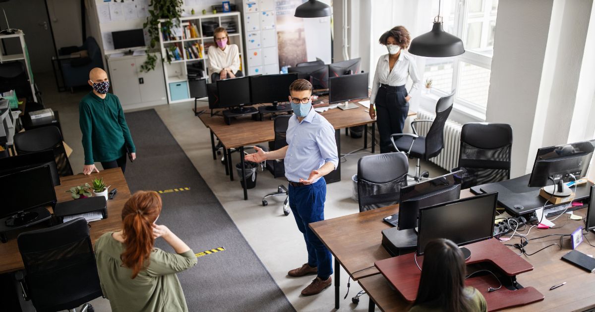 This stock image depicts office workers speaking while in masks.