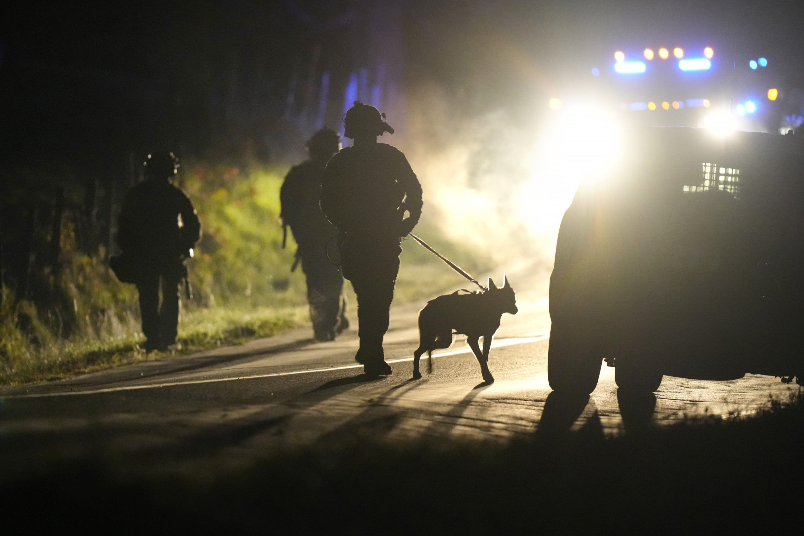 A member of law enforcement walks with a police dog outside a property on Meadow Road in Bowdoin, Maine, on Oct. 26.