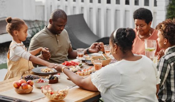 An undated stock photo shows a family holding hands and saying grace before a meal.