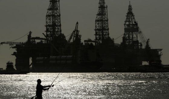 a man fishing near docked oil drilling platforms