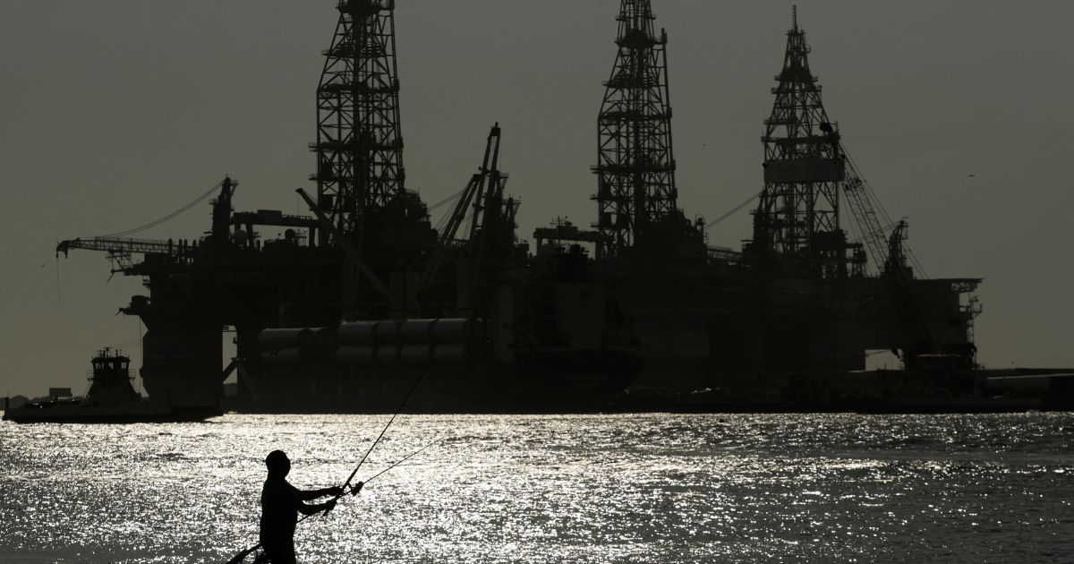 a man fishing near docked oil drilling platforms