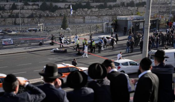 People watch as Israeli police officers and volunteers from the Zaka rescue service work the scene of a terrorist attack in Jerusalem on Thursday. Two gunman opened fire on a crowded bus station at the entrance of the city.