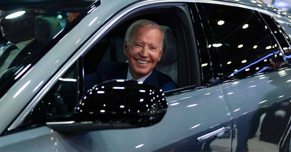 Joe Biden not looking where he's going as he drives a Cadillac Lyriq through a showroom