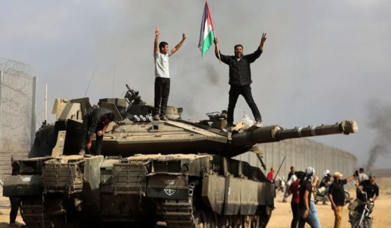 Palestinians waving their flag and celebrating by a destroyed Israeli tank