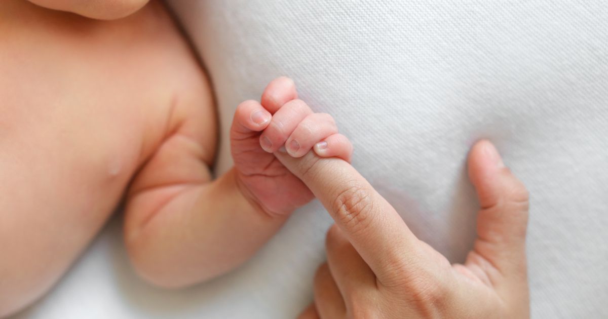 A baby holds a woman's finger in this stock image.