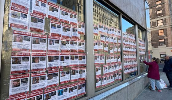 a woman hanging posters of individuals kidnapped by Hamas in Israel to the windows of a vacant store in New York City