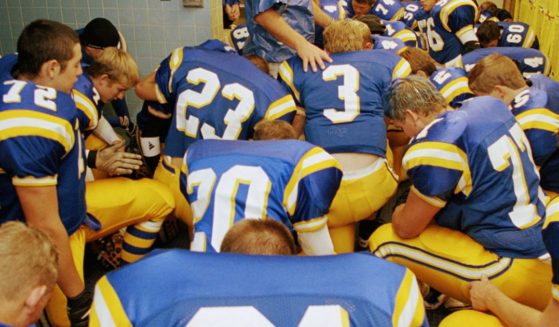 This stock image shows a high school football team praying before a game.