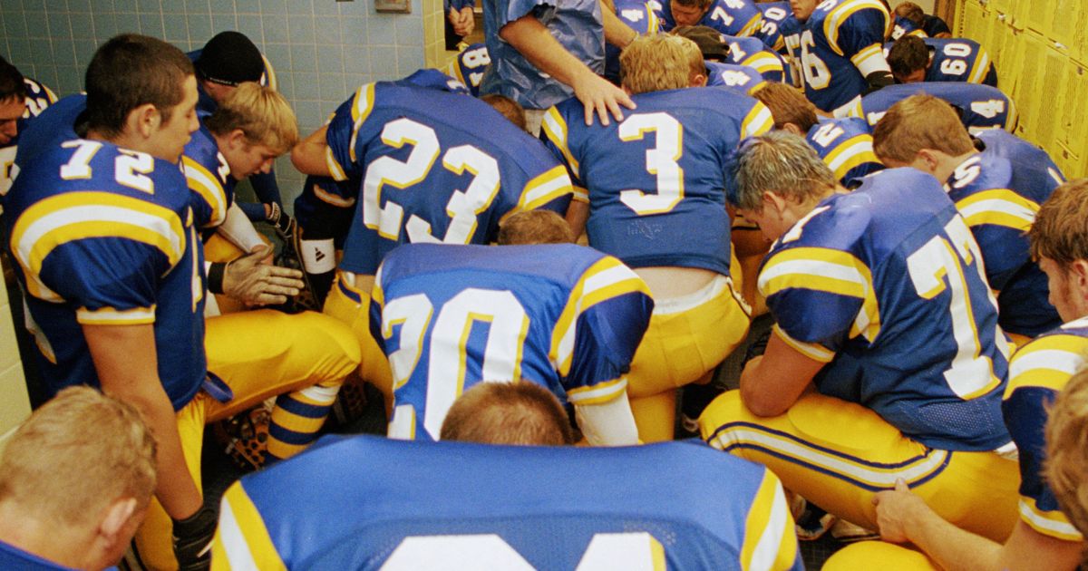 This stock image shows a high school football team praying before a game.