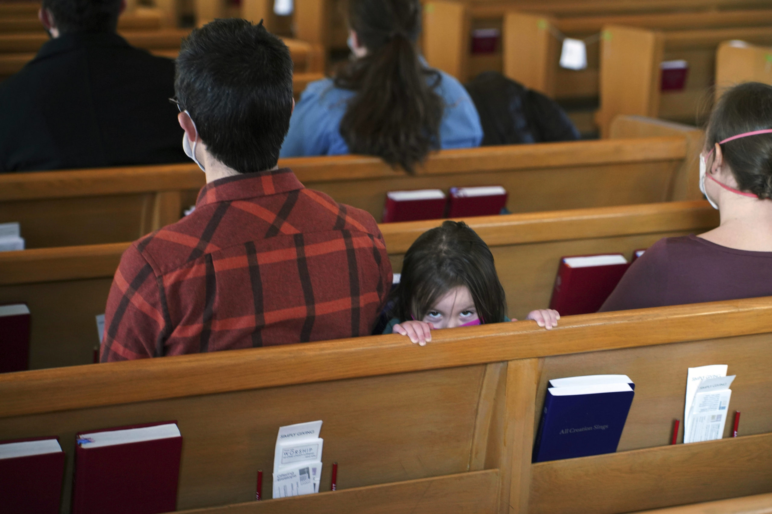 A young girl peeks above the pew next to her parents during services at Christ Church Lutheran, Jan. 23, 2022, in Minneapolis. (Jim Mone / AP)