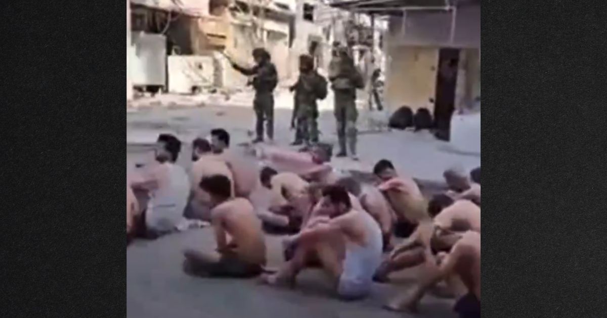 Prisoners sat on the street, stripped to their underwear, as they waited to be loaded onto truck.