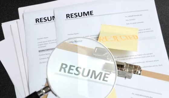 A stock photo shows resumes under a magnifying glass.