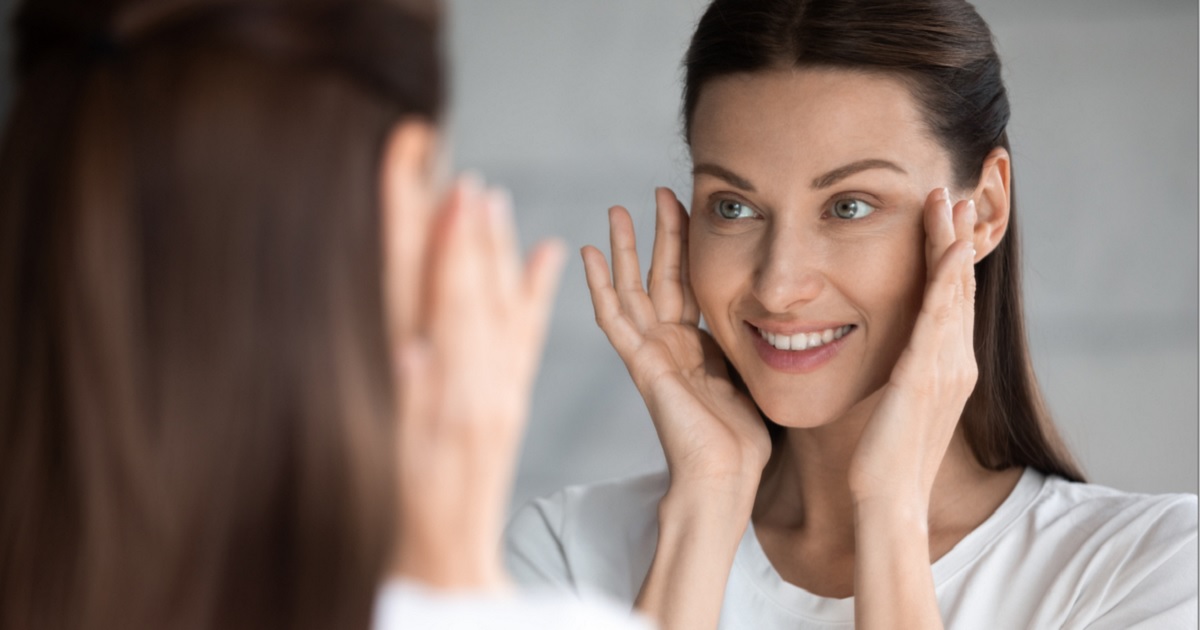 An attractive woman looks in the mirror apparently checking for wrinkles.