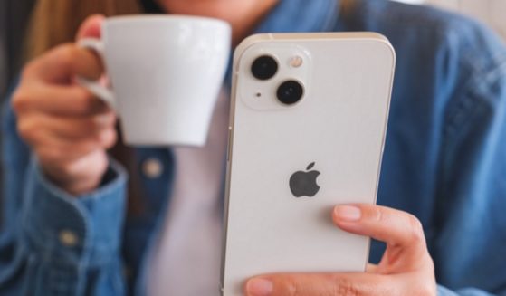 A woman drinking from a coffee mug and reading on her iPhone.