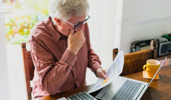 An elderly man looks at his bills in this stock image.