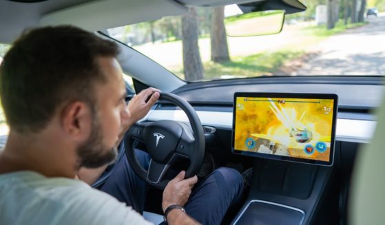 A man looks at the dashboard while driving a Tesla in this stock image.