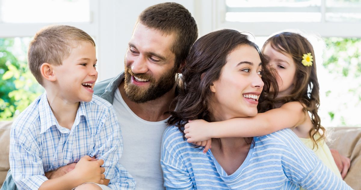A stock photo shows a couple and their children playing together on the sofa.