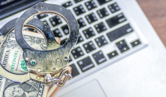 This stock image shows a wad of cash with handcuffs on a laptop.