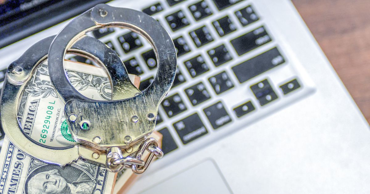 This stock image shows a wad of cash with handcuffs on a laptop.